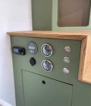 Panneau de commande avec jauges de niveau, prises et commandes intégré au mobilier du van aménagé.