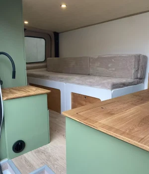 Espace de vie avec banquette convertible, cuisine en chêne et mobilier sur mesure dans un van aménagé