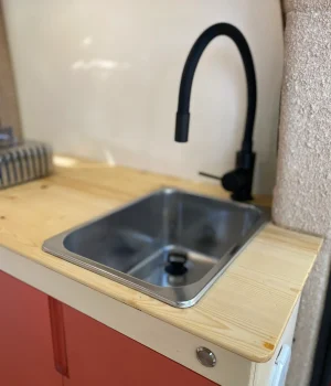 Évier en inox avec mitigeur noir mat sur plan de travail en bois dans un fourgon aménagé.