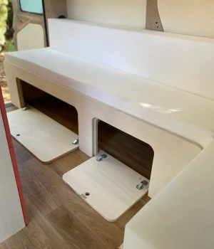 Coffres de rangement accessibles sous la banquette convertible d'un van aménagé.