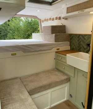 Aménagement complet de fourgon avec salon en L, lit sur soute, cuisine équipée avec évier et meuble haut de rangement.