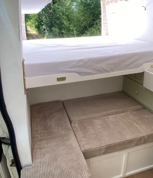 Lit peigne principal de 170 × 170 cm et lit banquette convertible de 125 × 90 cm déployés dans le fourgon aménagé.