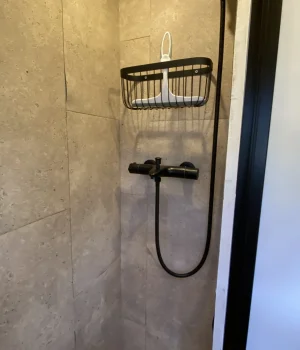 Douche à l'italienne avec colonne de douche, mur en travertin et sol en galets dans un fourgon aménagé.